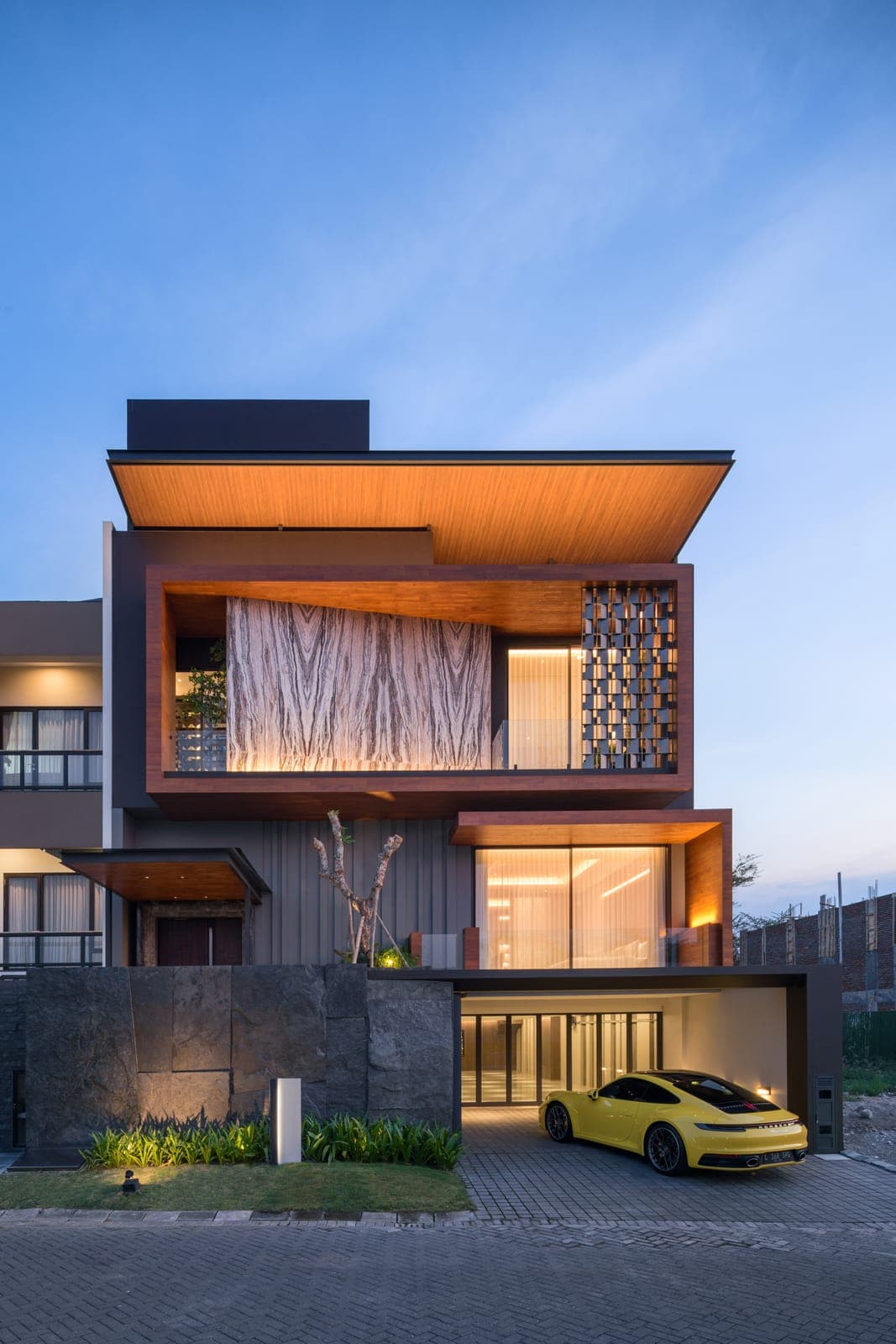 The street elevation at dusk — timber soffits folded over a base of split stone.