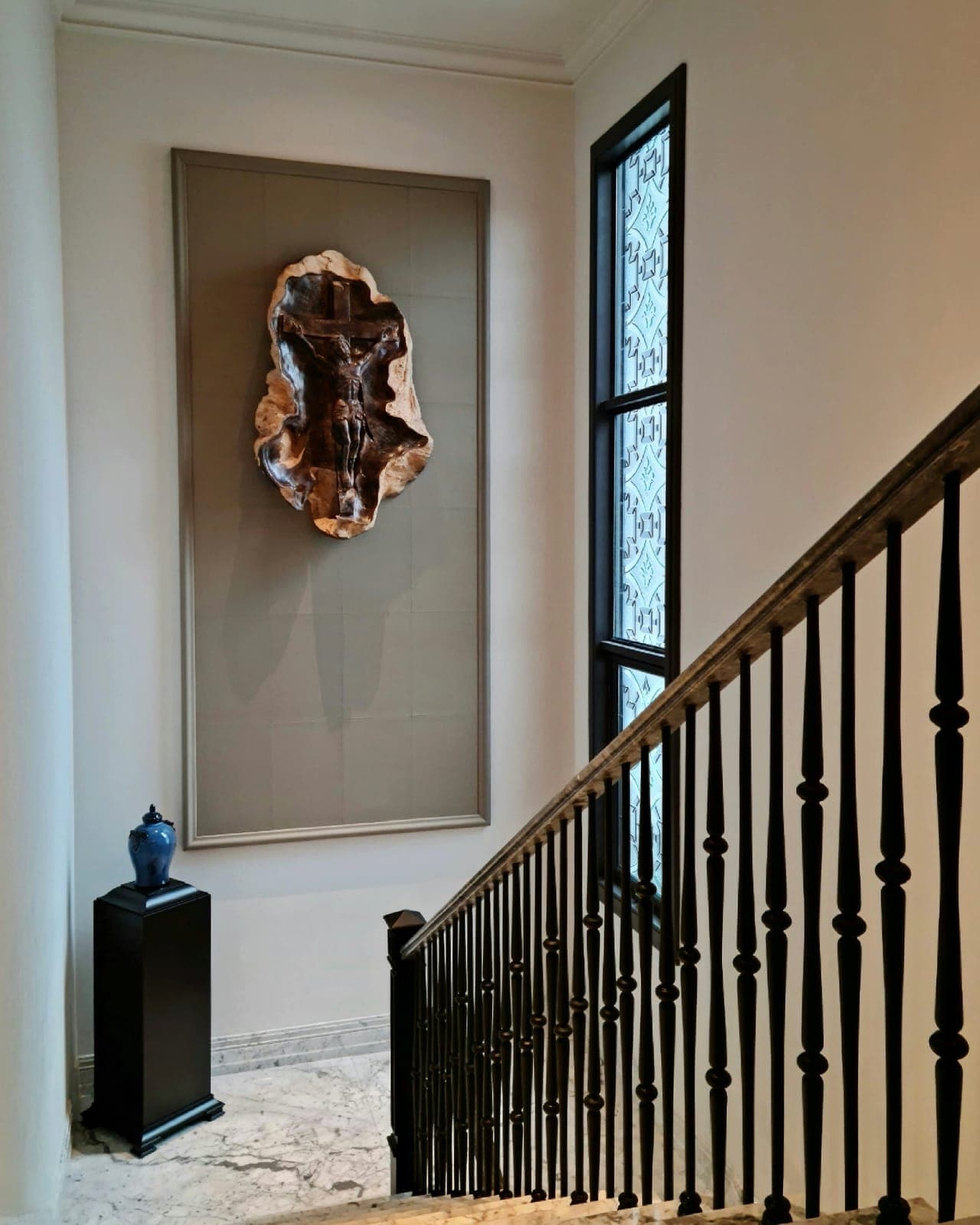The stair hall, one tall window of dark bars.