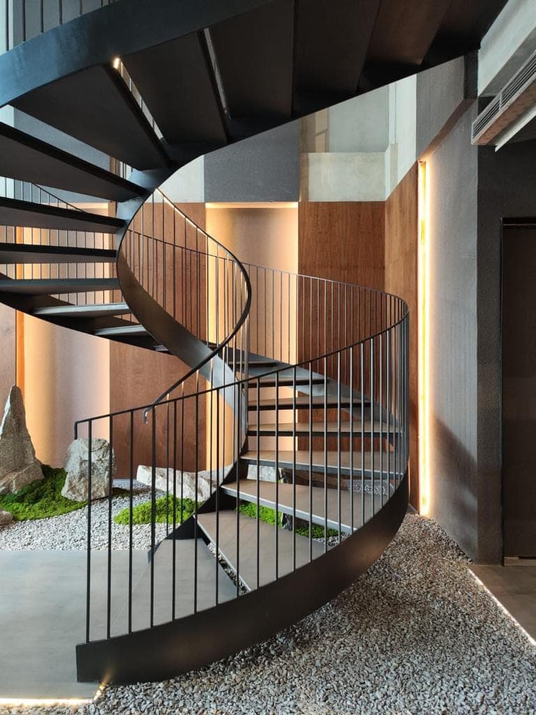 A steel spiral stair, set over a court of gravel, moss and stone.