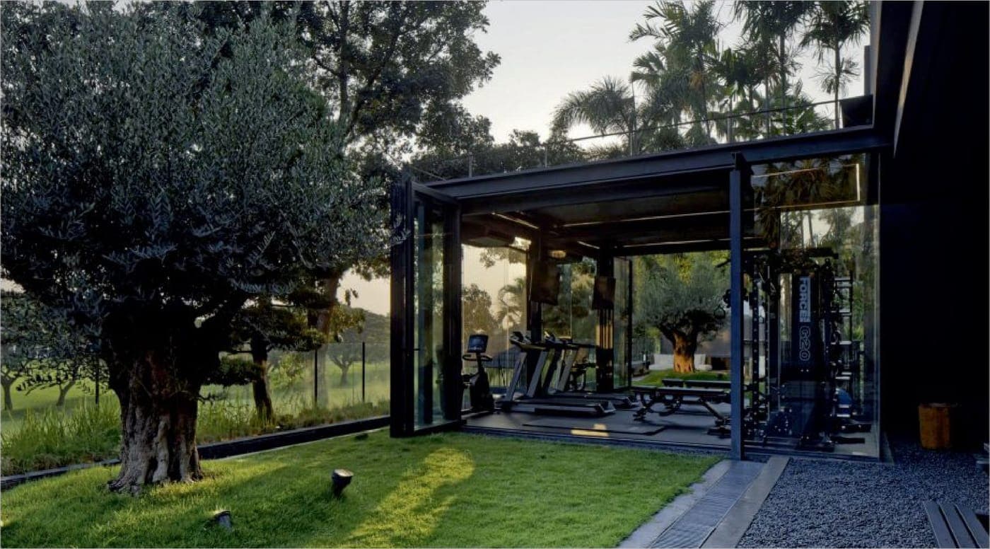A glass gymnasium folds fully open to the garden on the TECHNAL Ambial folding system.