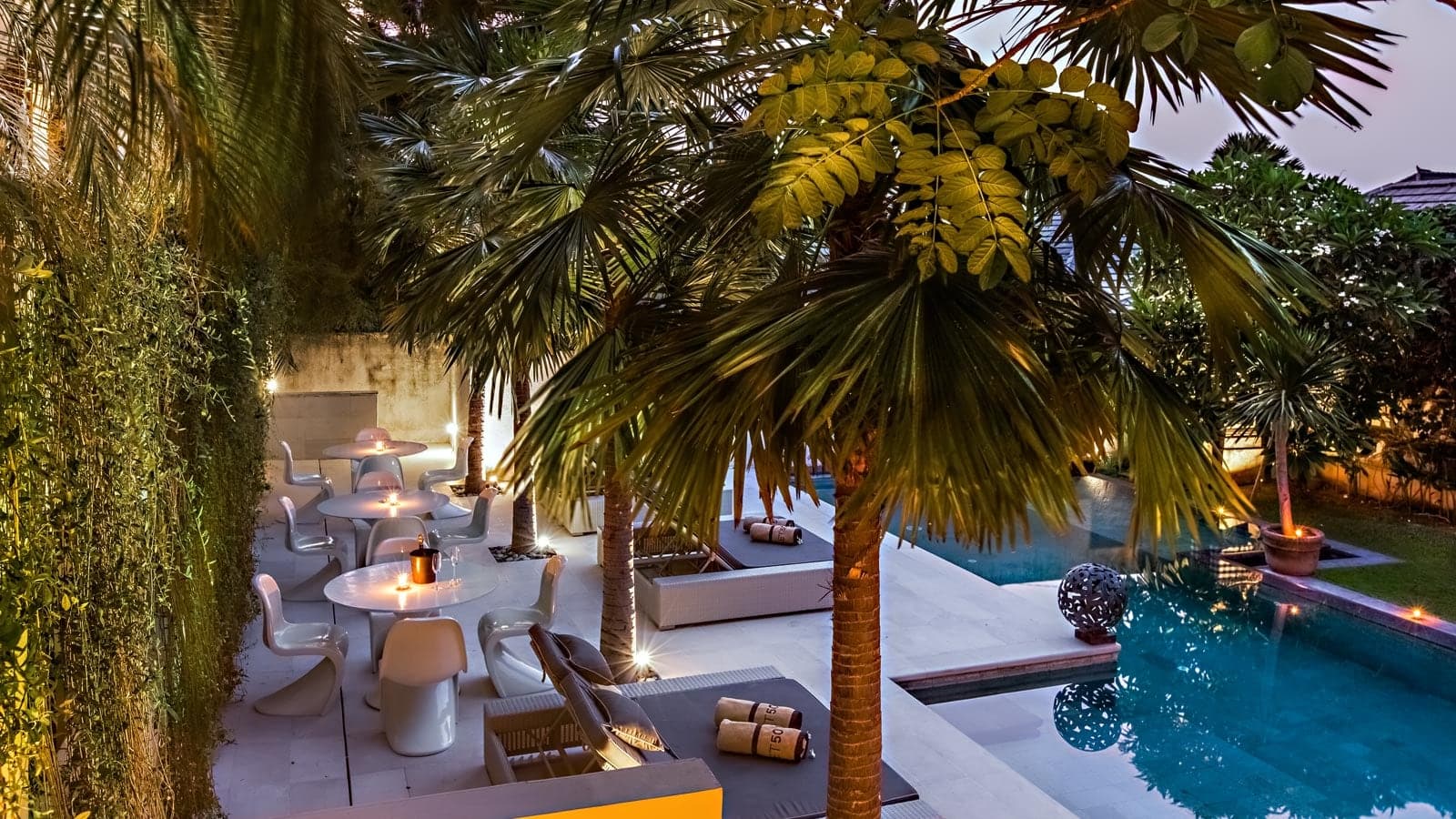 The same courtyard at dusk, the dining terrace lit under its green wall.