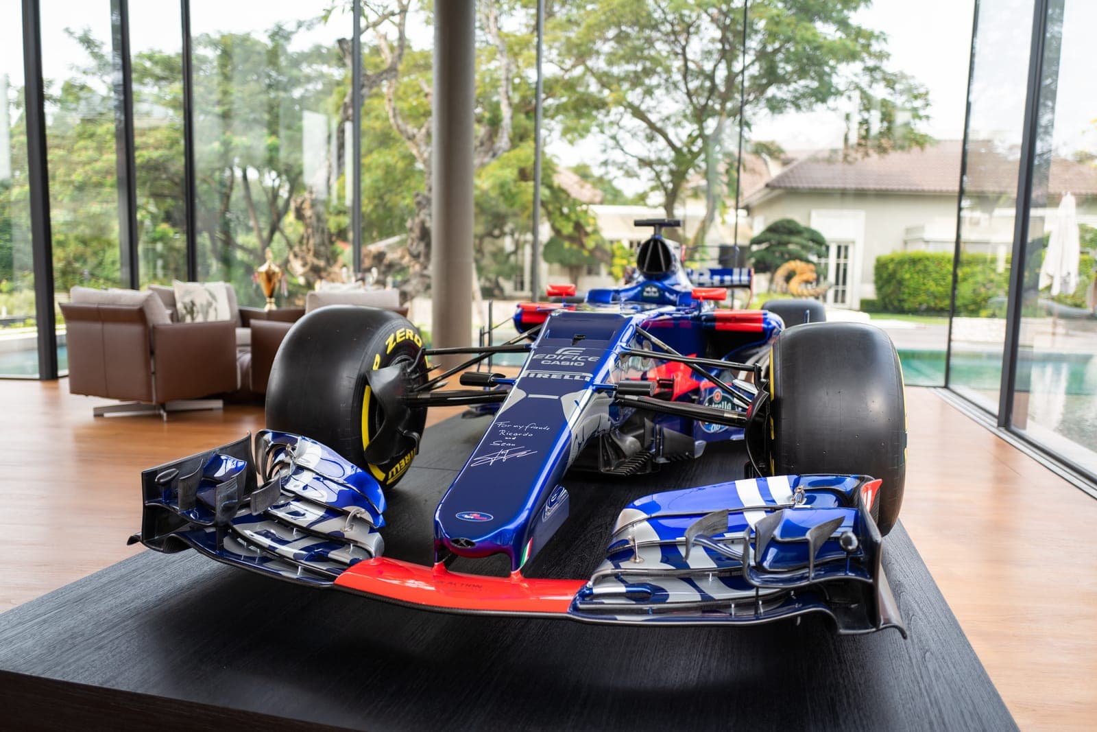 The gallery — a Formula 1 car framed against full-height glazing and the garden.