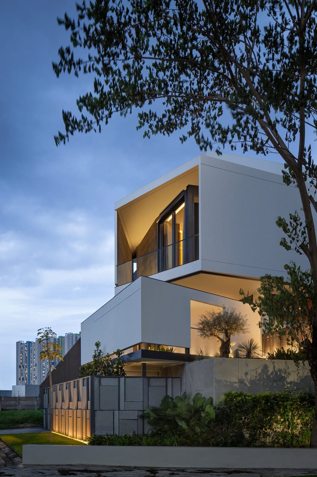 The street elevation at dusk: cantilevered white volumes over a stone base.